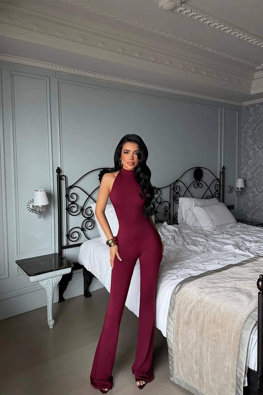 Femme portant une combinaison halter bordeaux dans une chambre chic.